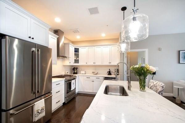 kitchen featuring stainless steel appliances, a sink, visible vents, white cabinets, and wall chimney range hood