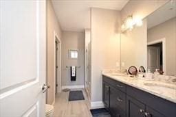 bathroom featuring double vanity, a stall shower, baseboards, wood finished floors, and a sink