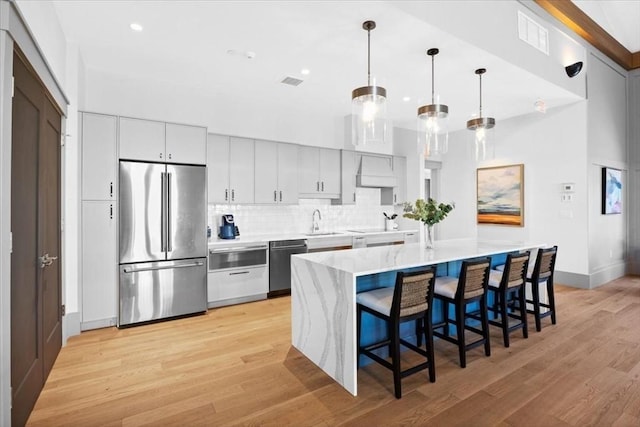 kitchen with light wood-style flooring, custom range hood, appliances with stainless steel finishes, and tasteful backsplash