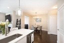 kitchen featuring dark wood-type flooring, decorative light fixtures, a sink, light countertops, and stainless steel dishwasher