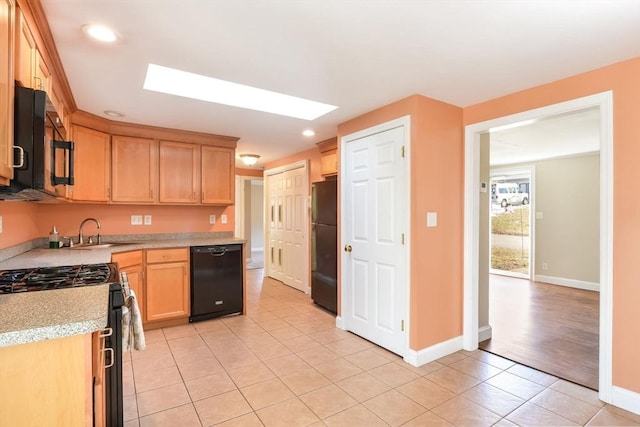 kitchen featuring light tile patterned floors, sink, a skylight, black appliances, and light brown cabinetry