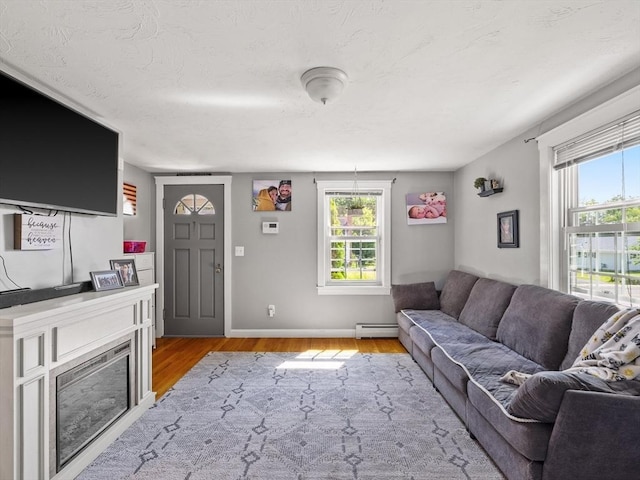 307 Boutelle St, Fitchburg, MA 01420 - living room with light wood-style floors, a baseboard heating unit, healthy amount of natural light, a glass covered fireplace, and a textured ceiling