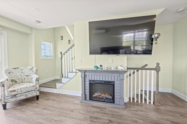living area featuring baseboards, wood finished floors, stairway, and a brick fireplace