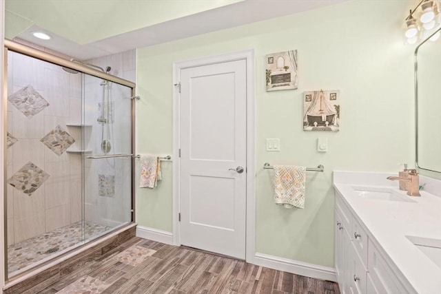 full bathroom with baseboards, a sink, a stall shower, double vanity, and wood finished floors