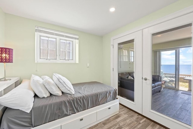 bedroom with recessed lighting, french doors, a water view, access to exterior, and wood finished floors
