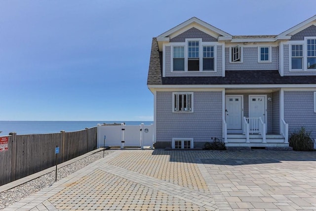 view of front of property featuring a gate, fence, a water view, and a shingled roof