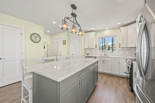 kitchen featuring a kitchen bar, appliances with stainless steel finishes, a sink, gray cabinets, and a center island