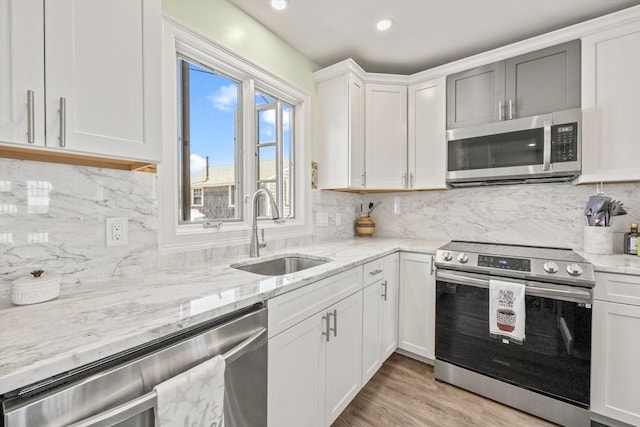 kitchen featuring white cabinetry, light wood-type flooring, stainless steel appliances, a sink, and light stone counters