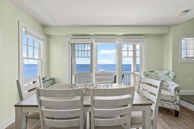 dining space with a water view, baseboards, and wood finished floors