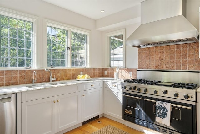 kitchen featuring appliances with stainless steel finishes, light stone counters, wall chimney exhaust hood, sink, and white cabinets