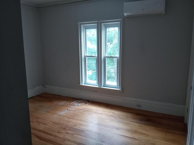 spare room featuring a wall mounted air conditioner, baseboards, and wood finished floors