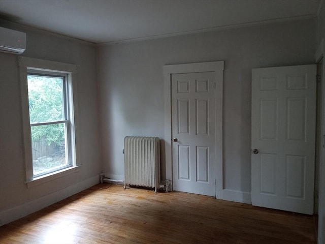 unfurnished bedroom featuring a wall mounted air conditioner, ornamental molding, wood finished floors, radiator heating unit, and baseboards