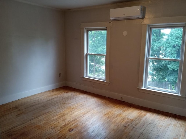 empty room featuring light wood finished floors, baseboards, a wall mounted air conditioner, and ornamental molding