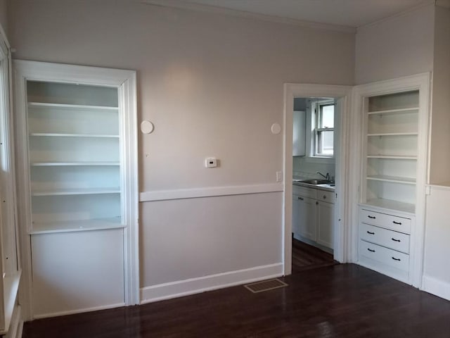 unfurnished dining area with visible vents, built in shelves, ornamental molding, dark wood-style floors, and a sink