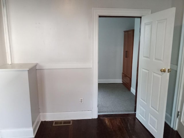 hallway with wood finished floors, visible vents, and baseboards