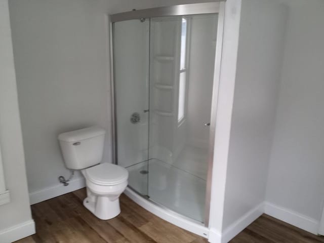 bathroom with a stall shower, baseboards, toilet, and wood finished floors