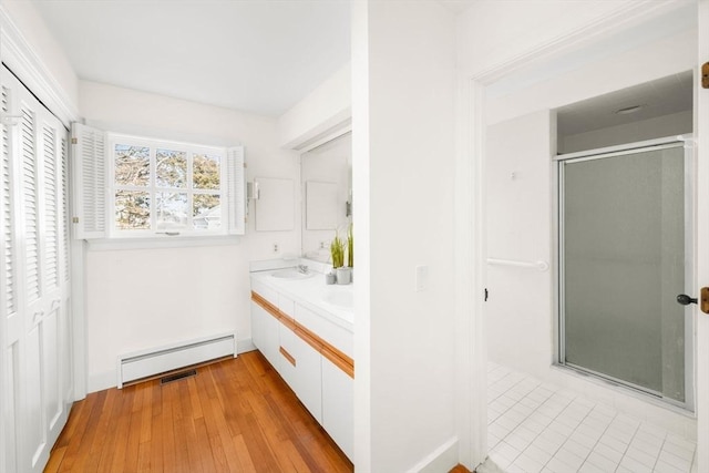 full bath featuring double vanity, a baseboard heating unit, a sink, a shower stall, and wood finished floors