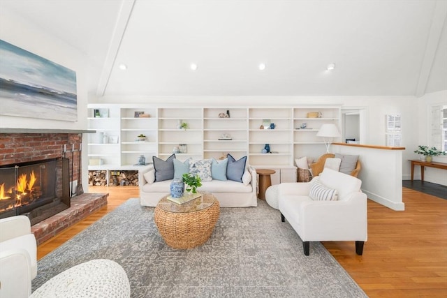 living room with a brick fireplace, lofted ceiling with beams, baseboards, and wood finished floors