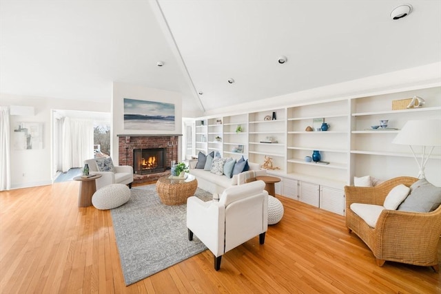 living room featuring lofted ceiling, a fireplace, built in features, and light wood-style floors