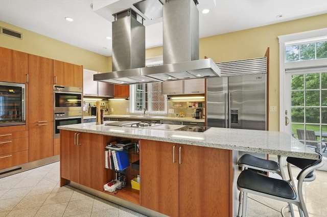 2 Azalea Way, Boxford, MA 01921 - kitchen with island range hood, stainless steel appliances, brown cabinets, open shelves, and a large island with sink