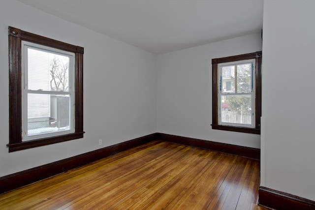 empty room with a healthy amount of sunlight, hardwood / wood-style flooring, and baseboards