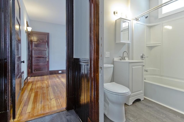 bathroom with toilet, wood finished floors, vanity, baseboards, and washtub / shower combination