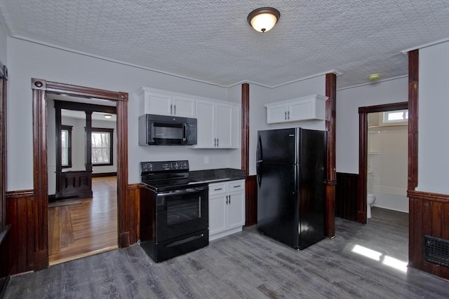 kitchen featuring dark countertops, black appliances, white cabinetry, and wainscoting