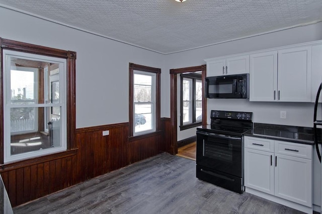 kitchen featuring a textured ceiling, a wainscoted wall, white cabinets, black appliances, and dark countertops