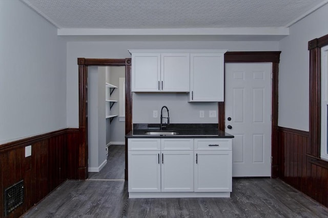 kitchen with dark countertops, a wainscoted wall, white cabinetry, and a sink