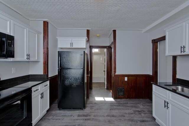 kitchen featuring dark countertops, wainscoting, white cabinets, and black appliances