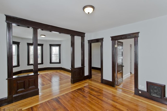 unfurnished room with light wood-style floors, ornate columns, visible vents, and baseboards