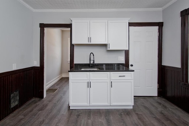 kitchen with a wainscoted wall, dark countertops, a sink, and white cabinets