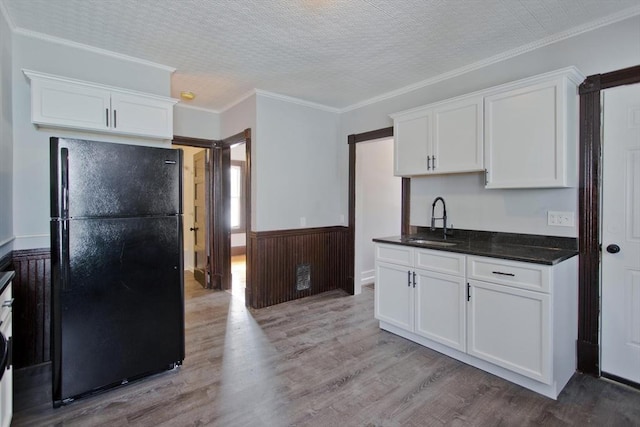 kitchen featuring wainscoting, white cabinetry, a sink, and freestanding refrigerator