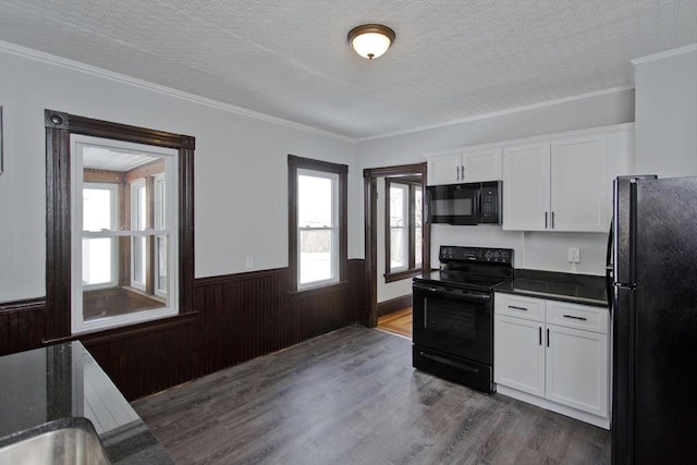 kitchen featuring dark countertops, black appliances, white cabinetry, and a wainscoted wall