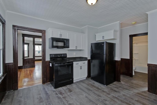 kitchen featuring dark countertops, a wainscoted wall, white cabinets, and black appliances