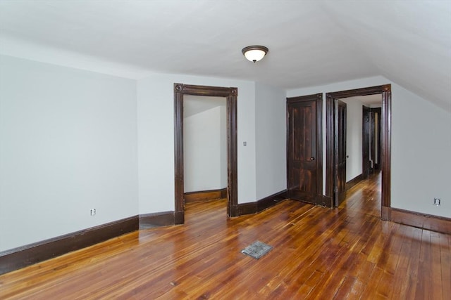 interior space featuring dark wood-type flooring, lofted ceiling, visible vents, and baseboards