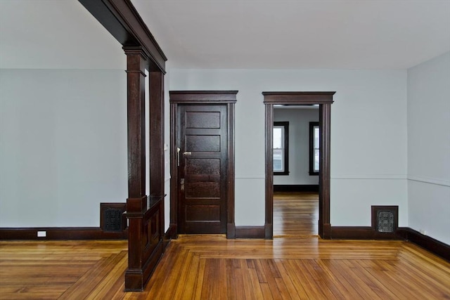 spare room with visible vents, hardwood / wood-style flooring, decorative columns, and baseboards