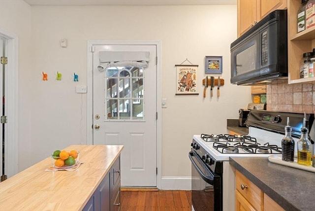 kitchen featuring backsplash, baseboards, black microwave, gas range oven, and wood finished floors