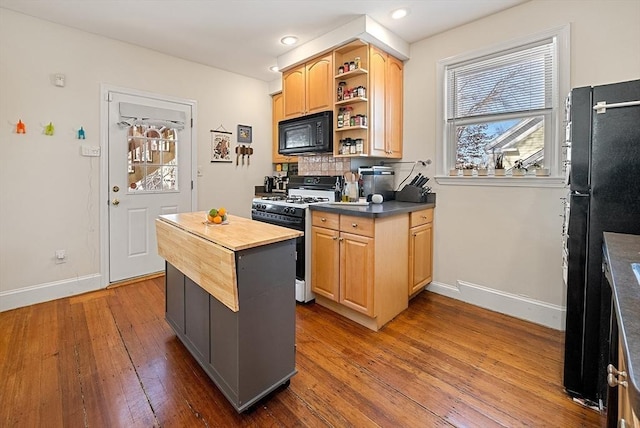 kitchen with baseboards, butcher block countertops, black appliances, hardwood / wood-style flooring, and tasteful backsplash