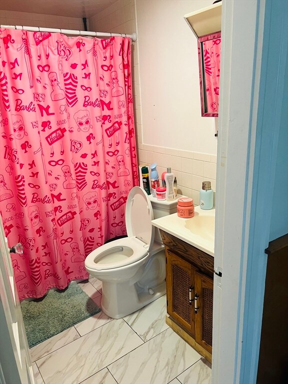 bathroom featuring tile walls, vanity, toilet, and walk in shower