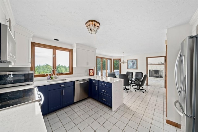 kitchen with a peninsula, white cabinets, stainless steel appliances, blue cabinets, and a sink