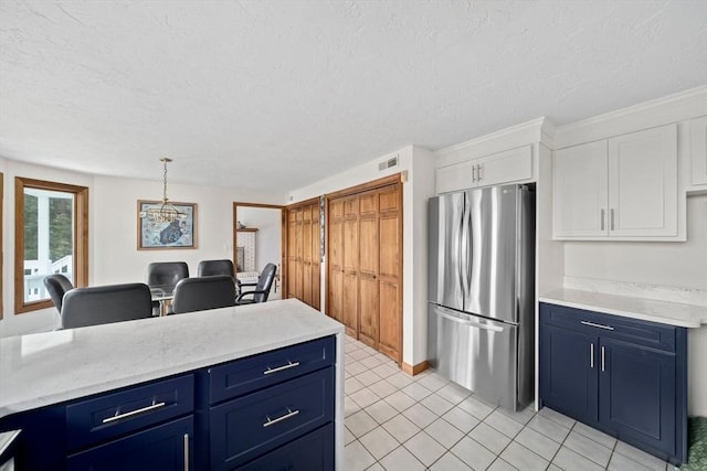 kitchen featuring blue cabinetry, a textured ceiling, white cabinets, and freestanding refrigerator