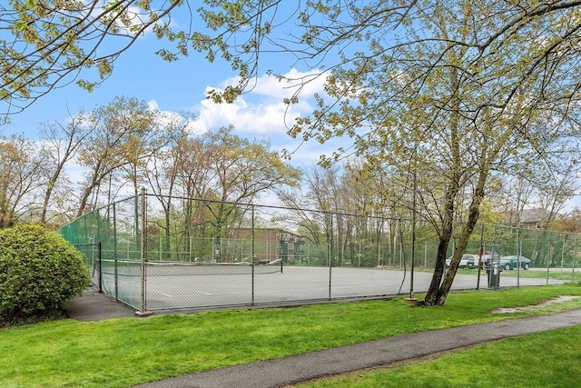 view of tennis court with a yard and fence