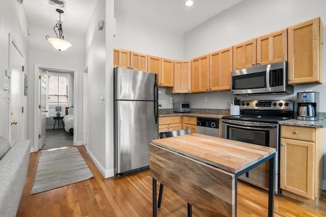 kitchen with light brown cabinetry, light wood-style floors, a high ceiling, hanging light fixtures, and stainless steel appliances