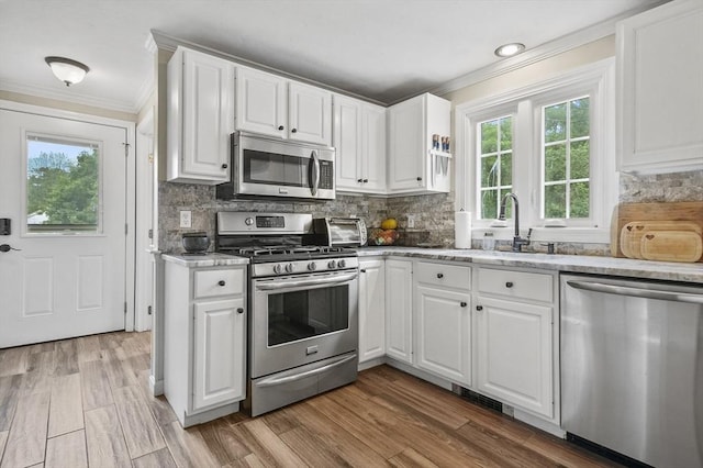 323 School St, Pembroke, MA 02359 - kitchen featuring appliances with stainless steel finishes, crown molding, white cabinets, tasteful backsplash, and light wood-style floors
