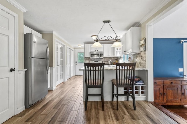 323 School St, Pembroke, MA 02359 - kitchen with appliances with stainless steel finishes, wood finished floors, a peninsula, white cabinets, and backsplash