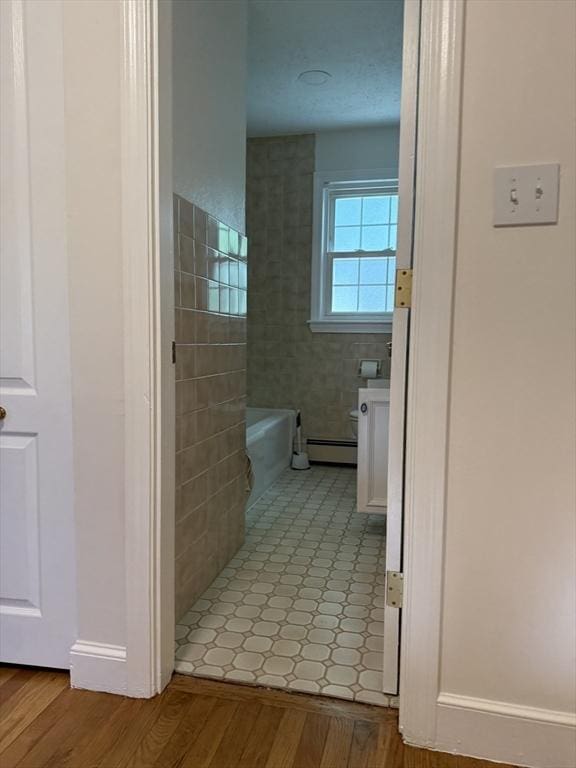 full bathroom with a bathtub, a baseboard radiator, and wood finished floors