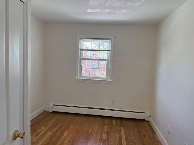 unfurnished room with baseboard heating, wood finished floors, and baseboards