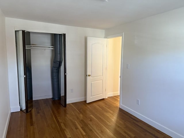unfurnished bedroom featuring wood finished floors, baseboards, and a closet