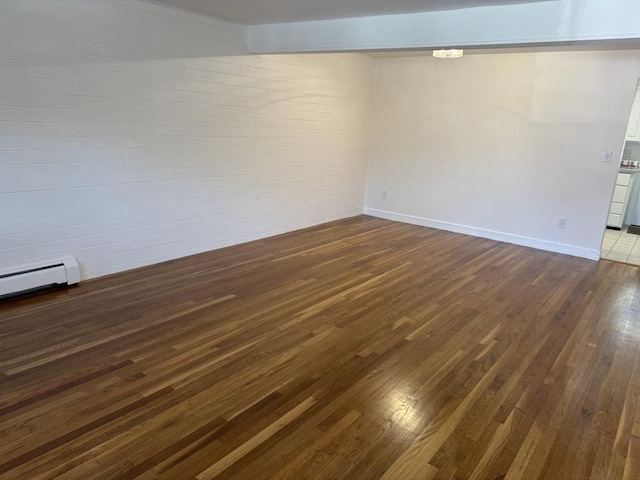 spare room featuring dark wood-type flooring, brick wall, and baseboards